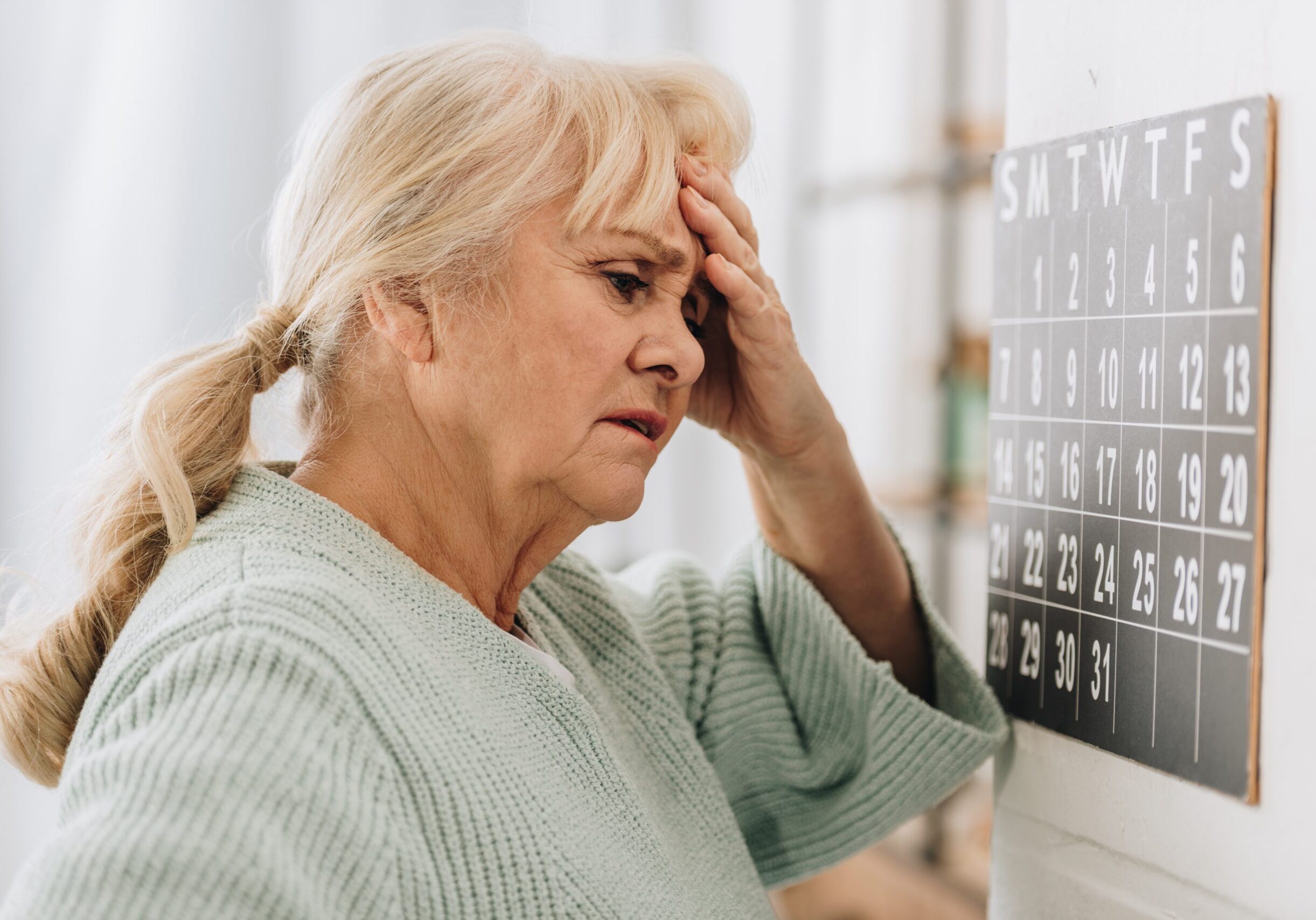 upset woman with gray hair touching head and looking at wall calendar Cognitieve training